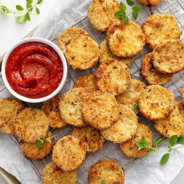 Breaded air fryer zucchini chips on a parchment-lined baking sheet.