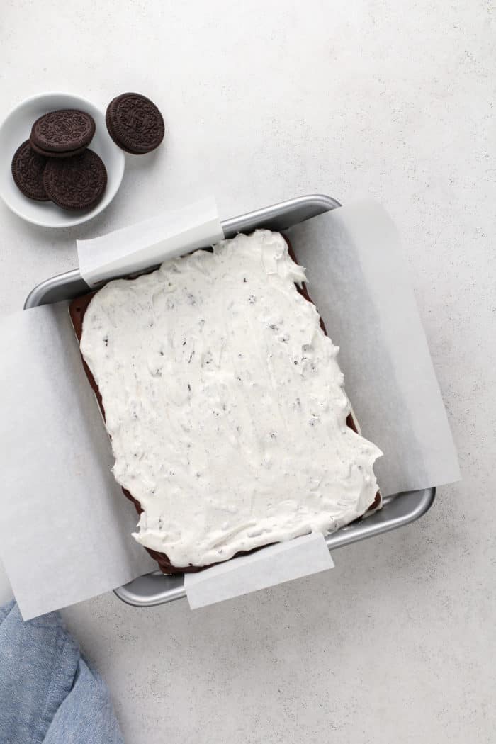 Oreo cool whip spread over hot fudge sauce and ice cream sandwiches in a square cake pan.