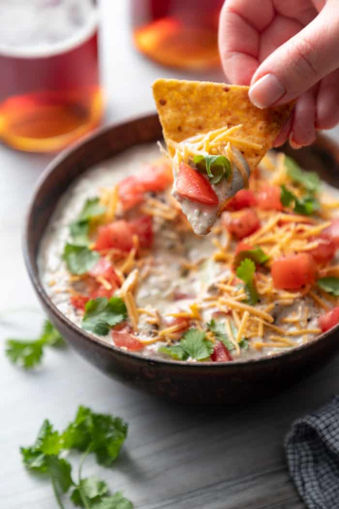 Hand holding up a tortilla chip that has been dipped in avocado dip.