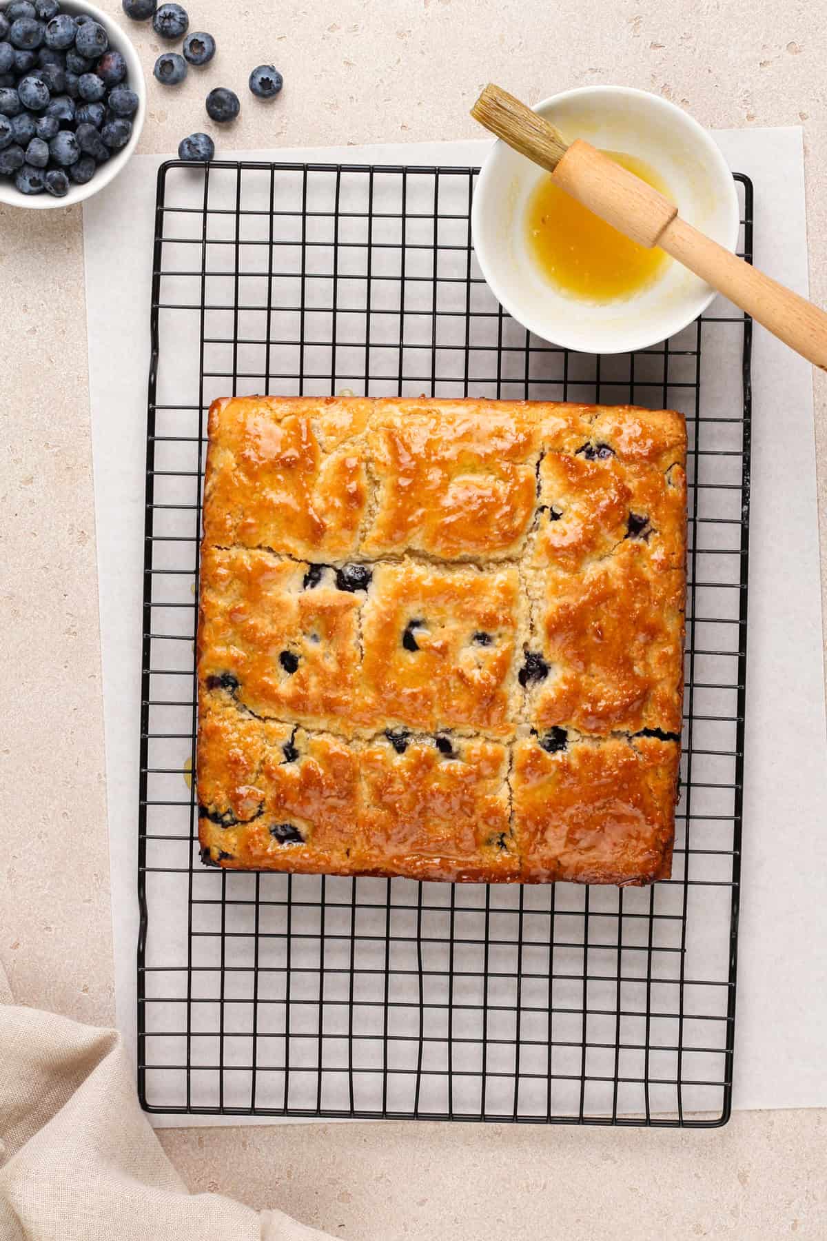 Baked blueberry biscuits on a wire cooling rack next to a bowl of honey butter.