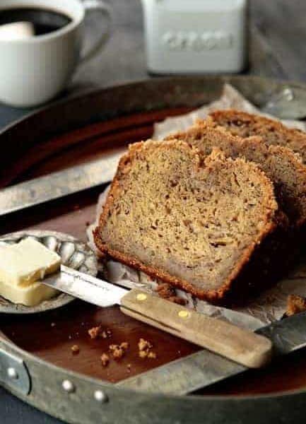 Sliced banana bread on a serving tray next to butter and a knife