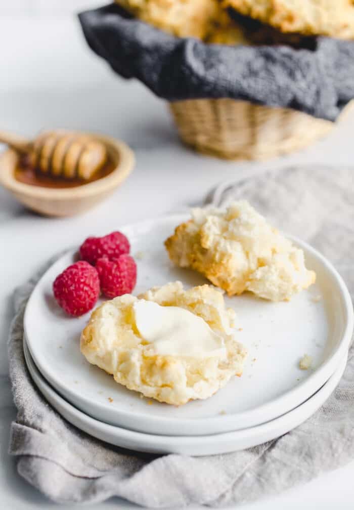 3/4 view of a butter-topped bisquick biscuit on a white plate, in front of a basket of biscuits