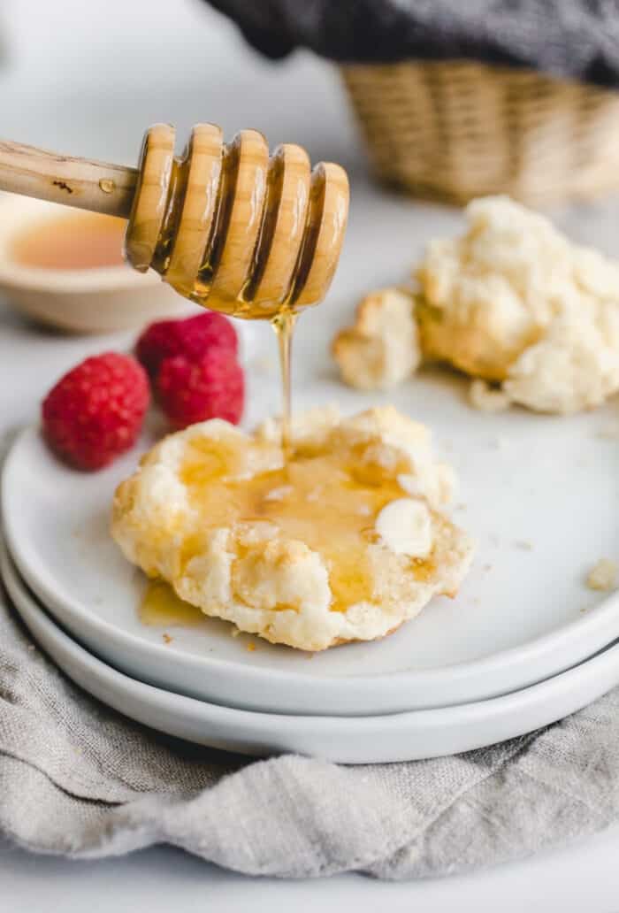 3/4 view of a wand drizzling honey over a bisquick biscuit on a white plate