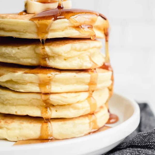 Syrup being drizzled over a stack of fluffy Bisquick pancakes on a white plate