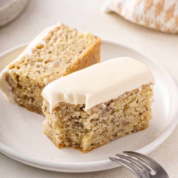 Halved slice of banana cake on a plate with a bite taken from the corner.