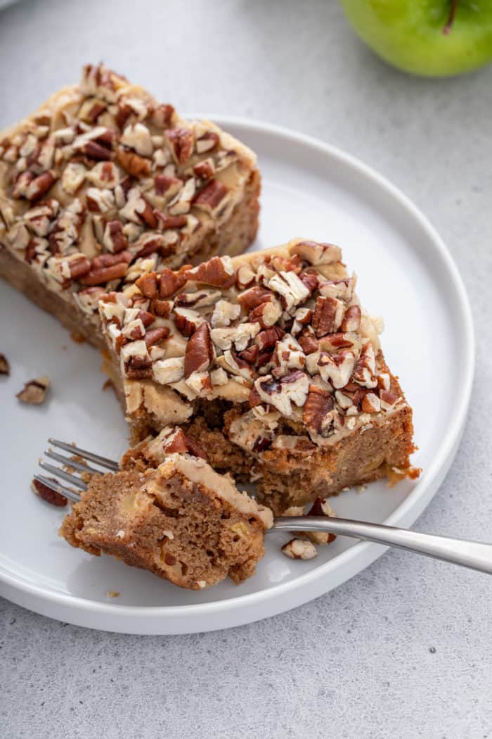 Two caramel apple blondies on a white plate. A fork has cut a corner from one of the blondies.