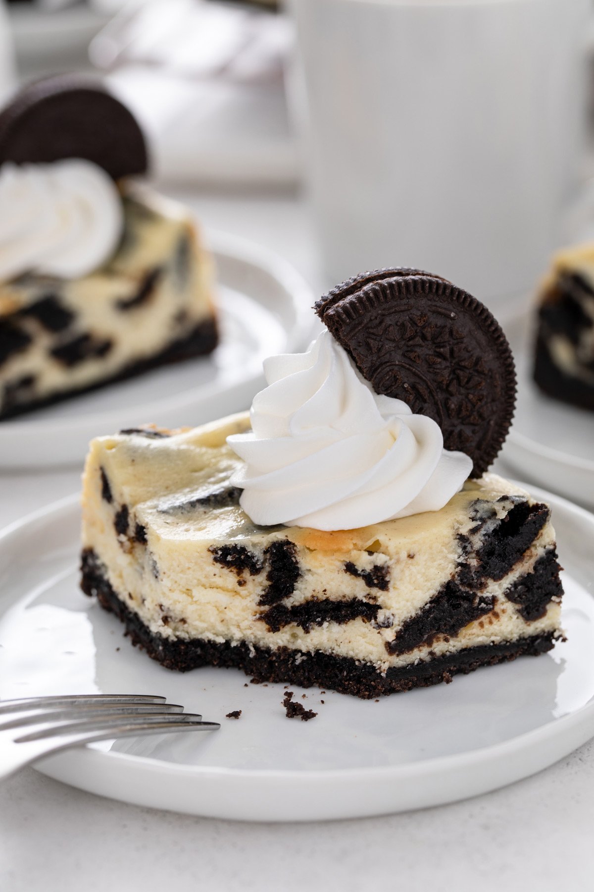 Plated oreo cheesecake bar with a bite taken from the corner of the bar. 