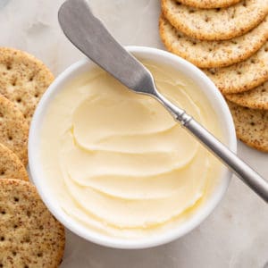 White bowl filled with homemade butter with a butter knife on the edge.