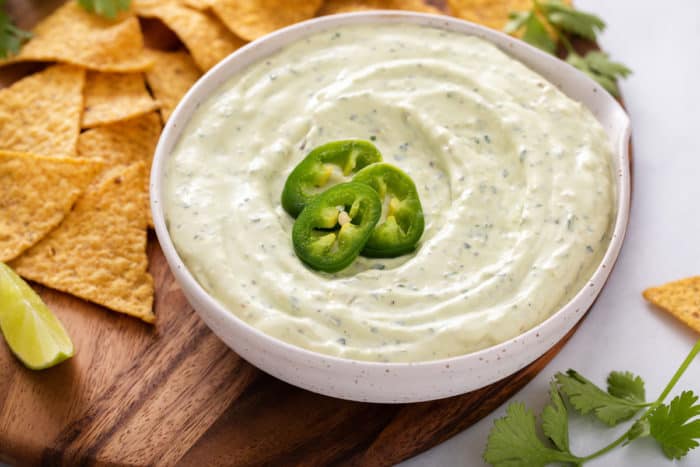 Jalapeño dip in a white bowl on a wooden board. Tortilla chips are on the board next to the bowl.