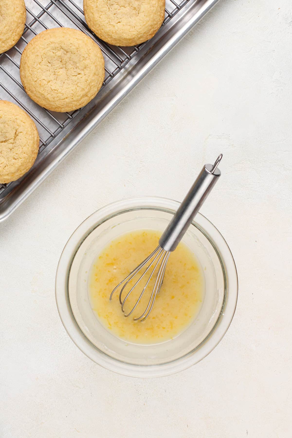 Bowl of lemon glaze next to cooling lemon cookies.