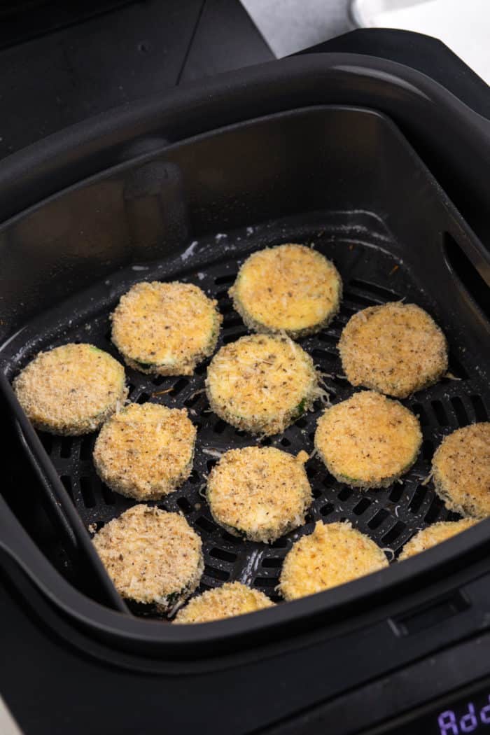 Breaded zucchini rounds in the basket of an air fryer.