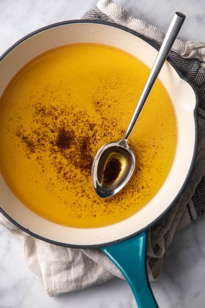 Brown butter and a spoon in a light colored skillet set on a tea towel.