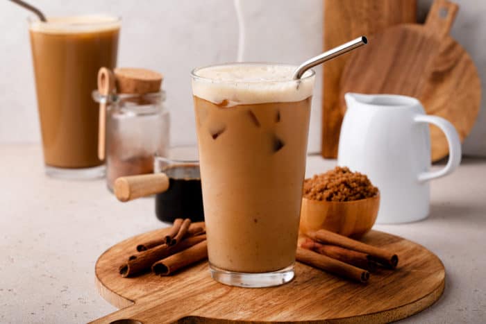 Glass of iced shaken espresso set on a wooden board and surrounded by brown sugar and cinnamon sticks.