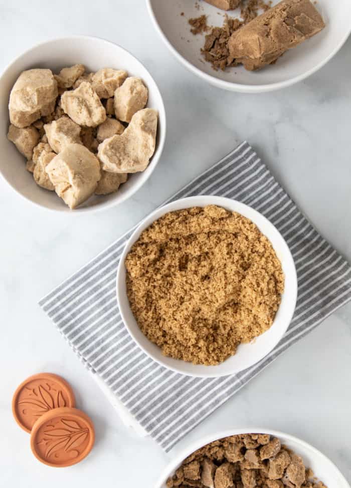 Several white bowls on a marble countertop filled with soft brown sugar and hard brown sugar clumps.