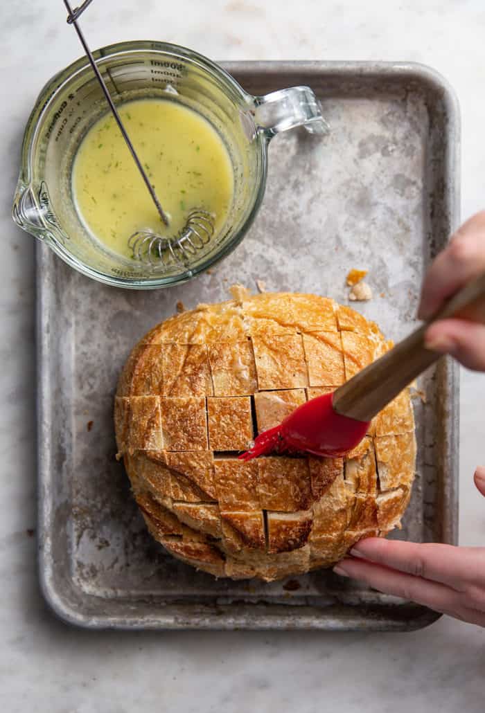 Hand brushing ranch butter into the cuts of a loaf of sourdough bread