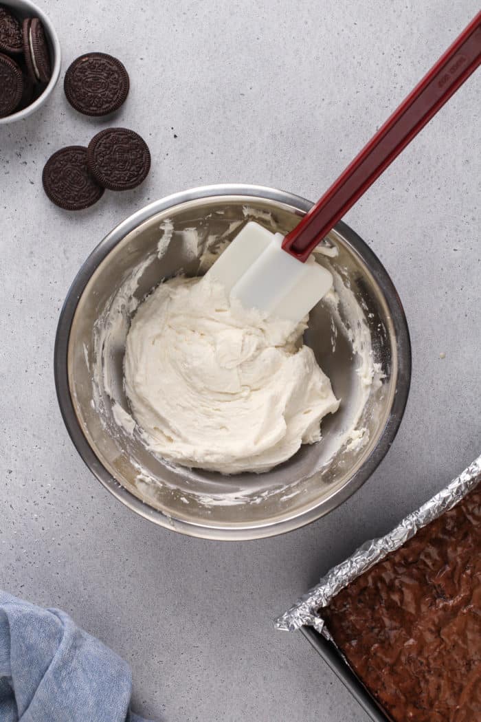 Bowl of vanilla buttercream frosting in a metal bowl, ready to be spread on top of baked oreo brownies.