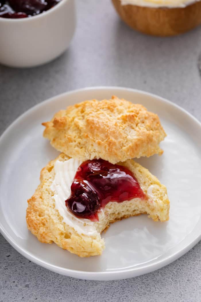 Bite taken from a buttermilk drop biscuit that has been split in half and topped with butter and berry jam.