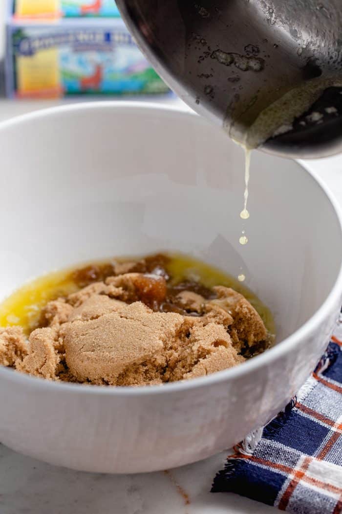 Pan pouring melted butter into a white bowl of brown sugar