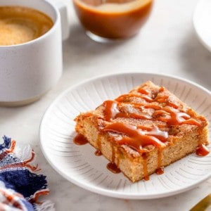 Apple bar drizzled with caramel sauce on a white plate with a cup of coffee and jar of caramel in the background