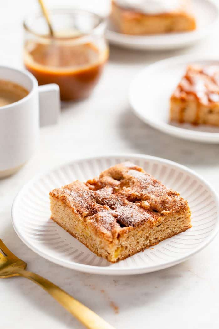 Apple bar on a white plate with coffee, caramel and more plated apple bars in the background