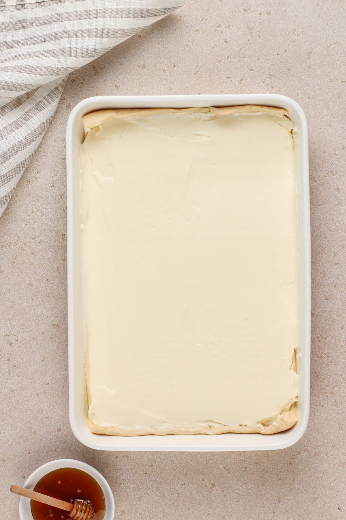 Cheesecake filling spread on top of a layer of crescent roll dough in a white pan.