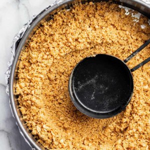 Measuring cup pressing mixture for graham cracker crust into a springform pan