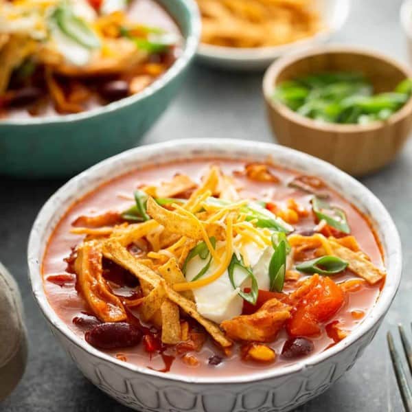 Close up of chicken chili topped with sour cream and cheese in a white bowl