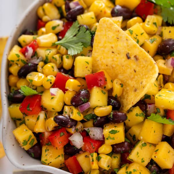 Tortilla chip in a bowl of mango and black bean salsa.