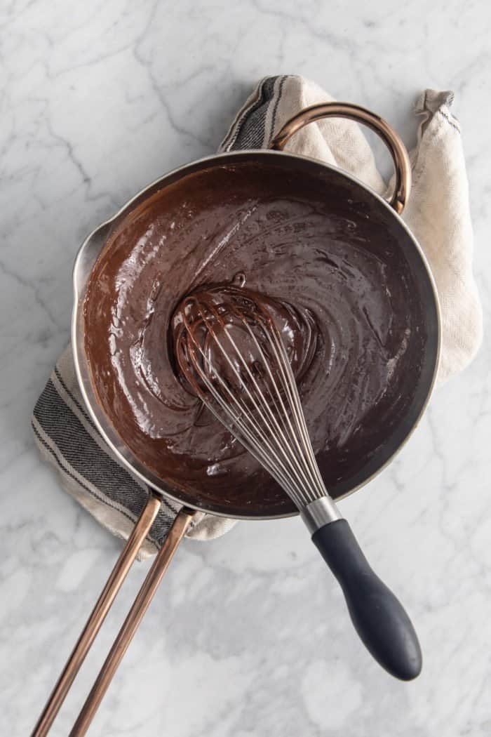 Chocolate and condensed milk being whisked in a saucepan.