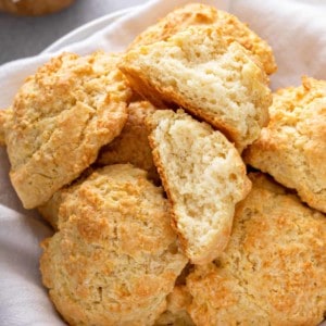 Close up of buttermilk drop biscuits in a basket. One of the biscuits is broken in half to show the light and fluffy texture.