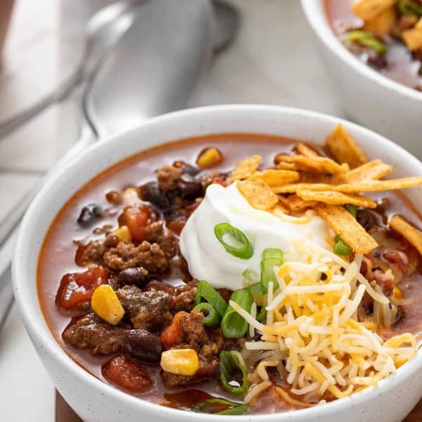 Close up of a white bowl filled with taco soup, garnished with sour cream, cheese, and tortilla strips