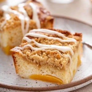 Two slices of easy peach coffee cake on a speckled plate. The bottom of a glass of milk is faintly visible in the background.