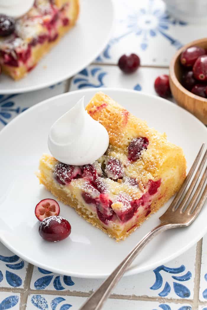 Close up of a cranberry gooey butter bar, topped with whipped cream, on a white plate