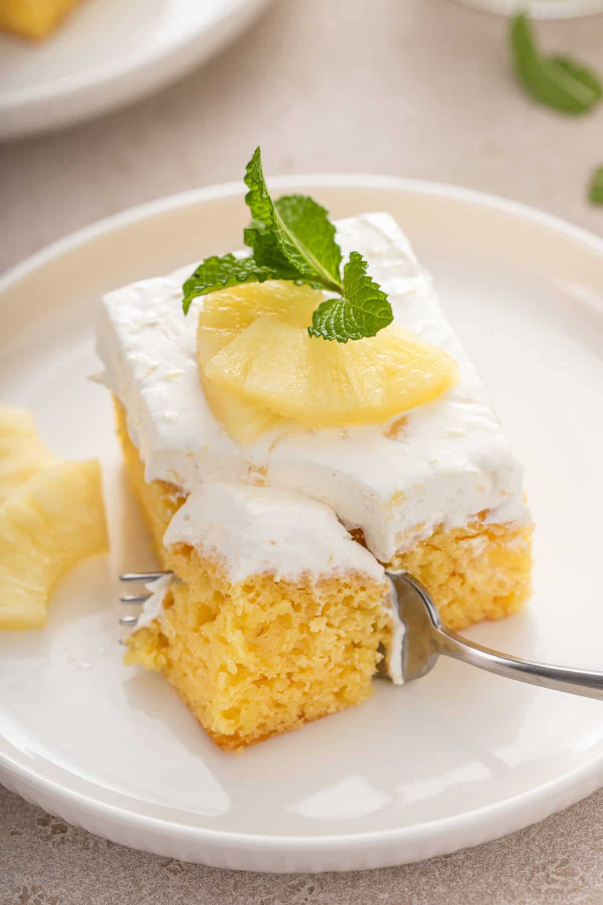 Fork taking a bite from the corner of a slice of pineapple cake on a white plate.