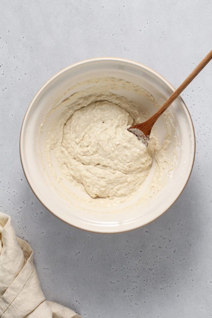 English muffin bread dough in a white mixing bowl, being stirred with a wooden spoon