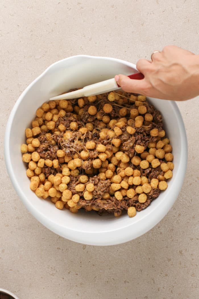 Cocoa krispies and peanut butter cap'n crunch cereal being folded into melted marshmallows.