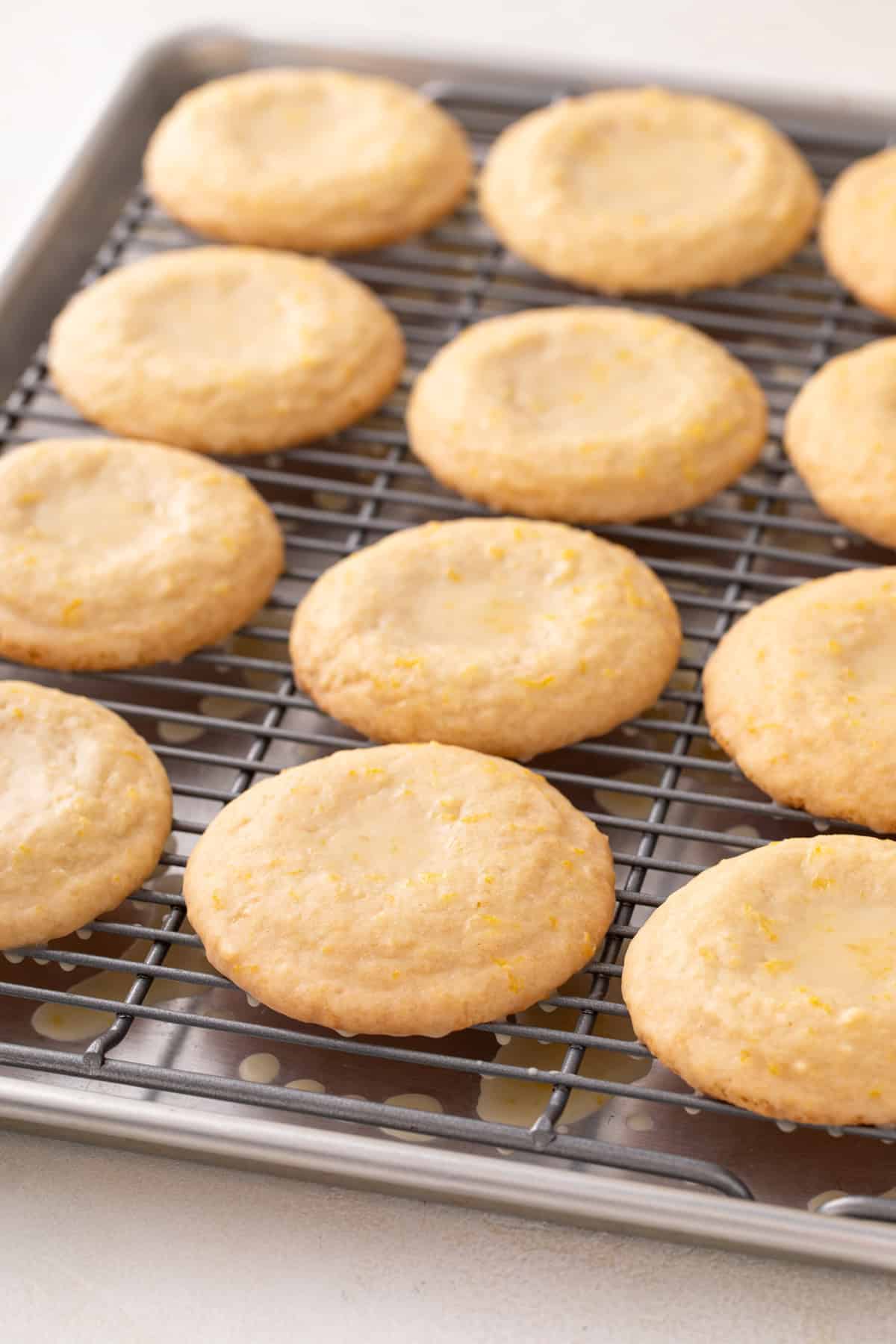 Freshly glazed lemon cookies lined up on a wire rack for the glaze to dry.