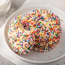 Funfetti cookie with a bite taken out of it leaning against a stack of 3 cookies on a plate