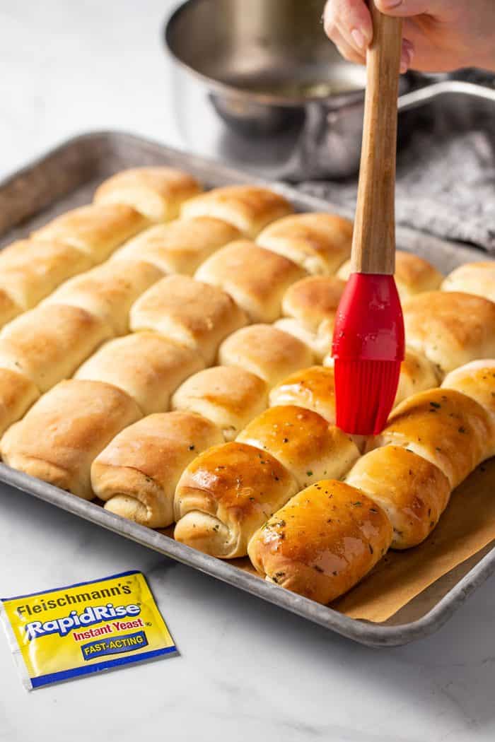 Pastry brush brushing herb butter onto freshly baked garlic and herb parker house rolls