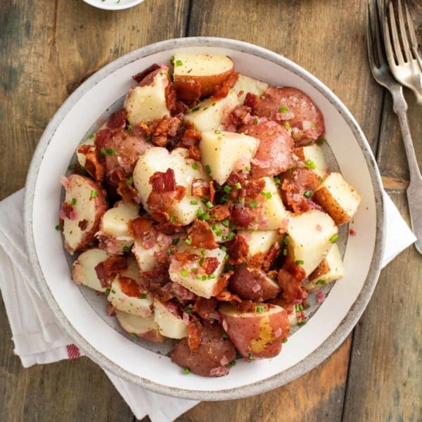 Overhead view of german potato salad in a serving bowl, set on a wooden table.