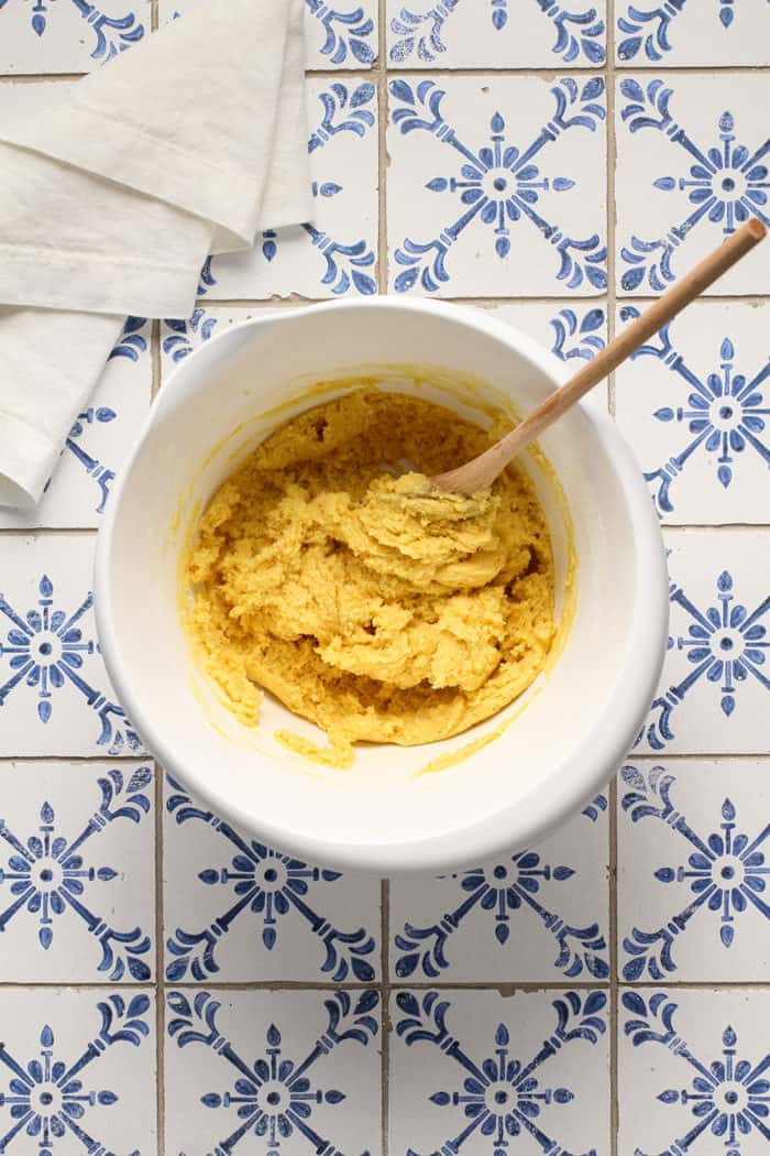 Wooden spoon stirring together the cake batter base for gooey butter bars in a white mixing bowl