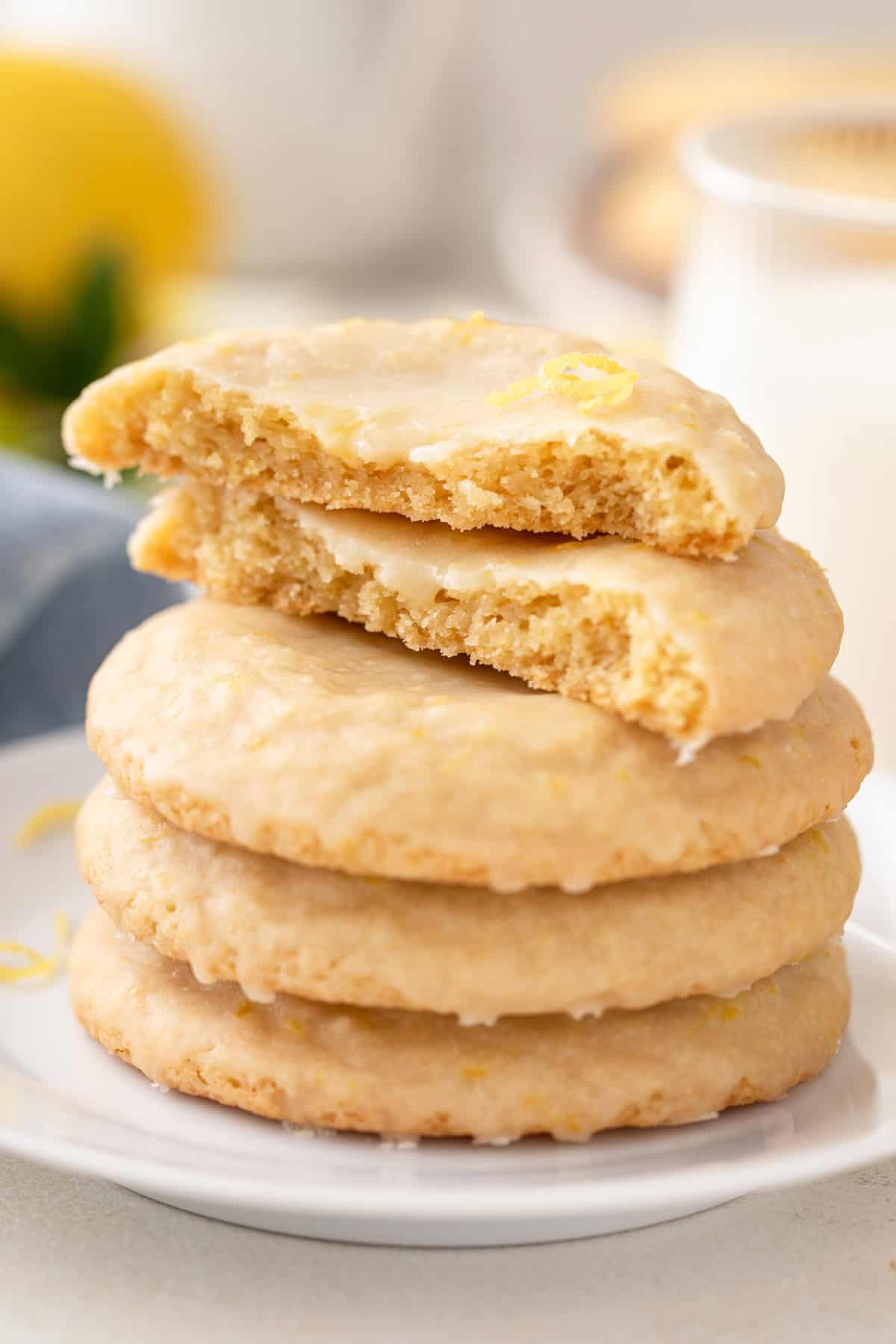 Three glazed lemon cookies stacked on a plate and topped with a halved cookie.