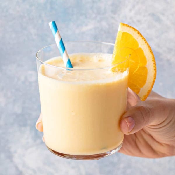 Hand holding up a glass of homemade orange julius.