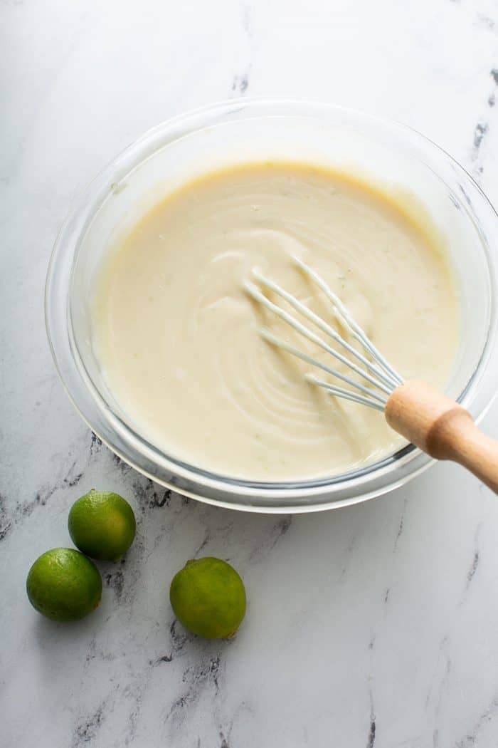 Key lime pie bar filling being whisked together in a glass mixing bowl on a marble surface