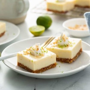 Key lime pie bars on a white plate with another plate of bars and a wire rack with more bars in the background