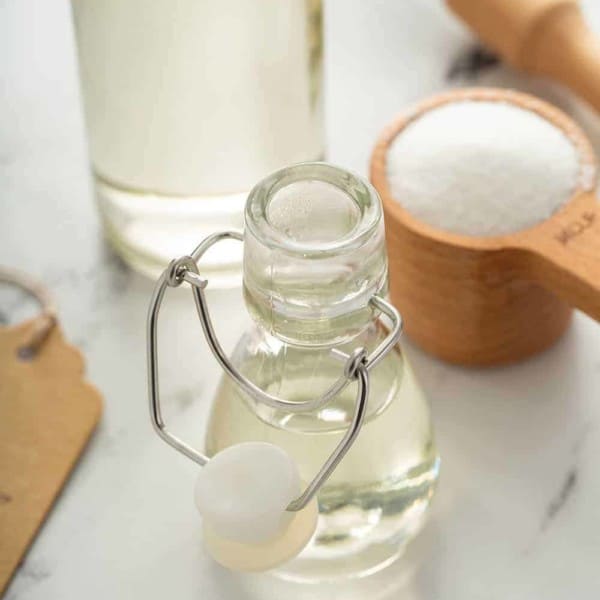 Small glass bottle of simple syrup on a marble counter with a measuring cup of sugar