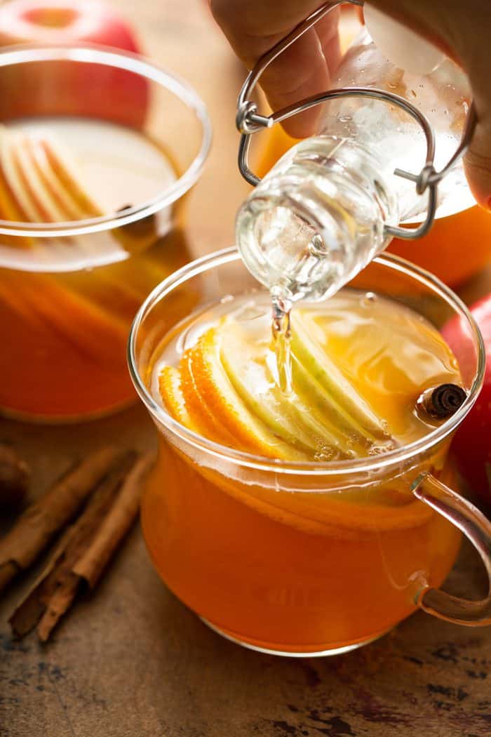 hand pouring simple syrup from a glass bottle into a mug of hot wassail