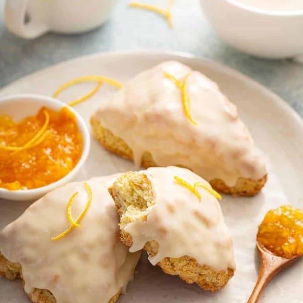 Orange scone with a bite taken out of it stacked on top of two other scones on a white plate