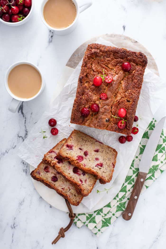 Overhead view of a loaf of sliced cranberry banana bread on a piece of parchment paper.