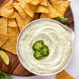 Bowl of jalapeño dip garnished with sliced jalapeños next to tortilla chips.